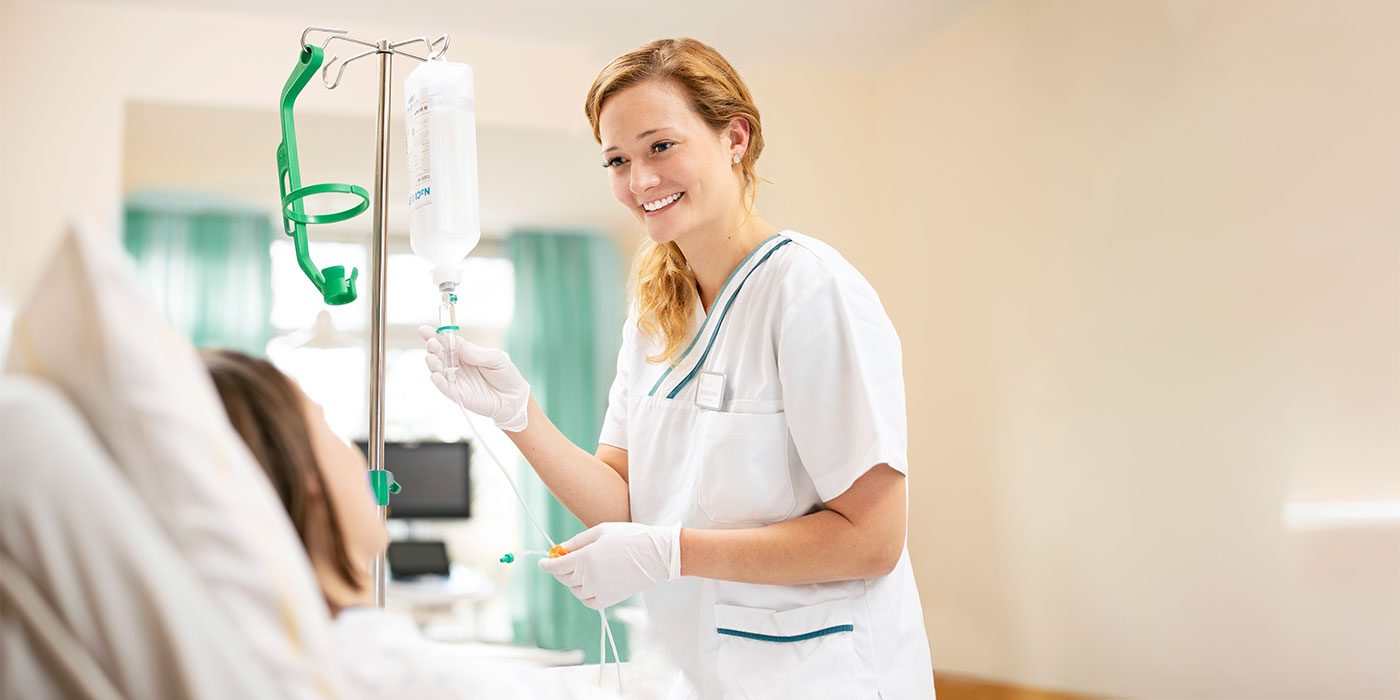 Eine l&auml;chelnde Pflegerin mit einem Tropf in der Hand